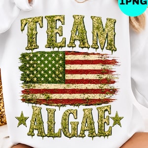 May include: A white sweatshirt featuring a graphic print with the text TEAM ALGAE in a textured green font. Between the words is a distressed American flag design with a mossy green overlay. Two green stars flank the word ALGAE on the bottom.
