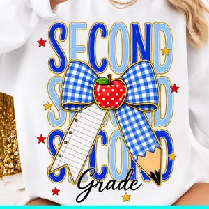 May include: A white sweatshirt featuring a graphic design with the text SECOND GRADE. The design includes a blue and white checkered bow, a red apple with white dots, a piece of lined notebook paper, a pencil, and small red and yellow stars.