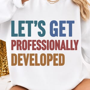 Könnte beinhalten: Ein weißes Langarm-Sweatshirt mit dem Text LET'S GET PROFESSIONALLY DEVELOPED in drei verschiedenen Farben. Die Wörter LET'S GET sind blau, PROFESSIONALLY ist rot und DEVELOPED ist braun, alles in einer fetten serifenlosen Schriftart.