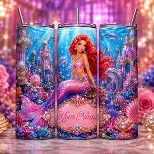 May include: A cylindrical metal tumbler with a straw featuring a vibrant underwater scene with a red-haired mermaid, dolphins, and a coral reef. The design includes a decorative pink frame with the placeholder text Your Name in cursive script.