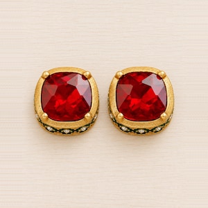 May include: A pair of square-shaped stud earrings featuring large, faceted deep red stones set in textured gold-tone metal. The sides of the settings are accented with a dark green enamel band and small, clear embedded stones in a repeating pattern.