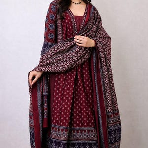 May include: A burgundy salwar kameez ensemble with a matching patterned shawl. The outfit features intricate floral and geometric designs in navy and white. The long-sleeved tunic and pants are adorned with a delicate dot pattern.