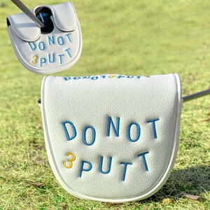 Pu&ograve; includere: Copertura bianca per la testa del putter da golf con testo ricamato blu che recita "DO NOT PUTT" e un "3" dorato. La copertura &egrave; su una superficie erbosa verde. La mazza da golf &egrave; inserita nella copertura.