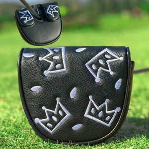 Pu&ograve; includere: Copertura per putter da golf nera con ricami bianchi a forma di corona. La copertura &egrave; realizzata in materiale strutturato e ha una chiusura magnetica. La copertura per putter &egrave; mostrata su uno sfondo erboso verde.