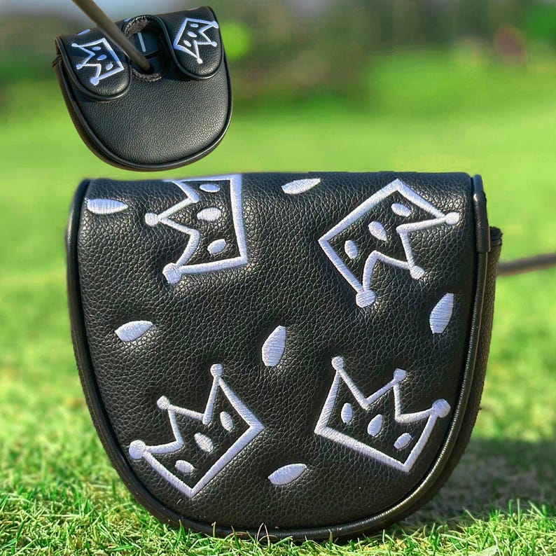Pu&ograve; includere: Copertura per putter da golf nera con ricami bianchi a forma di corona. La copertura &egrave; realizzata in materiale strutturato e ha una chiusura magnetica. La copertura per putter &egrave; mostrata su uno sfondo erboso verde.