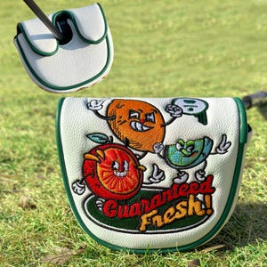 Pu&ograve; includere: Copertura per putter da golf bianca con finiture verdi e un design di frutta a cartoni animati. La copertura presenta un'arancia, un kiwi e un'anguria con la scritta "Guaranteed Fresh!" in rosso e verde.