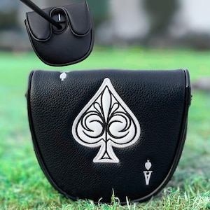 Może przedstawiać: Czarny pokrowiec na putter do kija golfowego z białym haftowanym wzorem Asa Pik. Pokrowiec wykonany jest z teksturowanej sk&oacute;ry i posiada magnetyczne zapięcie. Kij golfowy jest czarny.