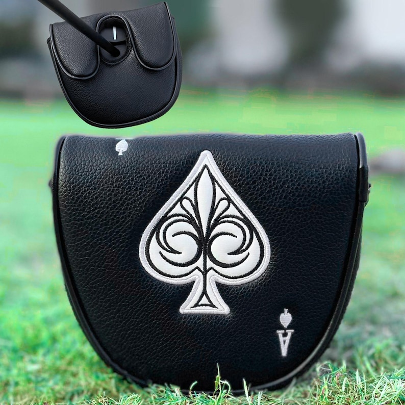 Może przedstawiać: Czarny pokrowiec na putter do kija golfowego z białym haftowanym wzorem Asa Pik. Pokrowiec wykonany jest z teksturowanej sk&oacute;ry i posiada magnetyczne zapięcie. Kij golfowy jest czarny.