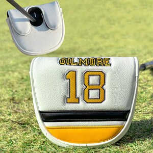 Pu&ograve; includere: Copertura bianca per la testa della mazza da golf con il nome "GILMORE" in lettere dorate e il numero "18" in oro con contorno nero. La copertura presenta un motivo a strisce nere e gialle nella parte inferiore. Una mazza da golf &egrave; inserita nella copertura.
