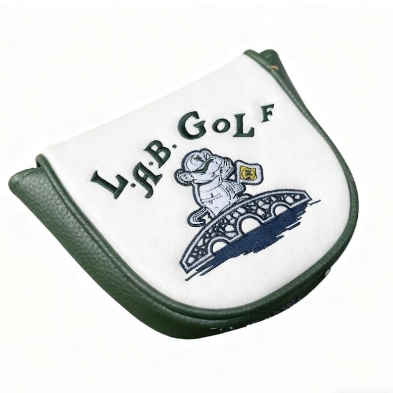May include: White golf club head cover with green trim. The cover features the text "L.A.B. Golf" in green and a cartoon illustration of a mouse on a bridge. The cover is made of a smooth, likely synthetic material.