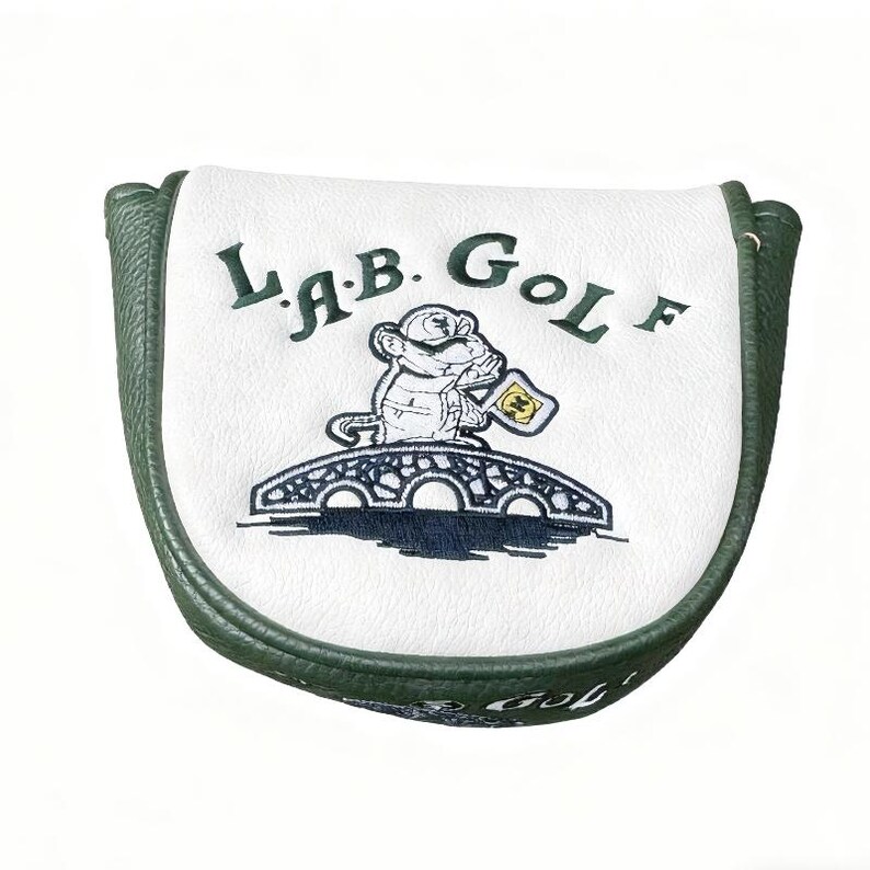 May include: A white and green golf club head cover with the text "LAB GOLF" and a cartoon monkey holding a flag. The cover has a green border and a white center with a bridge design.