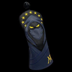 May include: A navy blue and black golf club head cover with a stylized ninja design. The cover features yellow star accents and yellow eyes. The letter "M" is embroidered in yellow on the side.