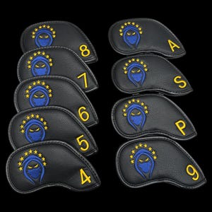 May include: A set of black golf club head covers. Each cover has a blue ninja design with yellow star accents and a yellow number or letter. The covers are displayed against a black backdrop.