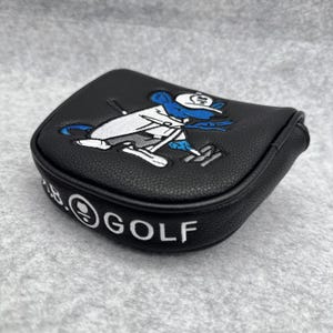 May include: Black golf club head cover with a cartoon mouse design in white, blue, and gray. The cover has the text "B.GOLF" in white. The cover is made of a textured material.