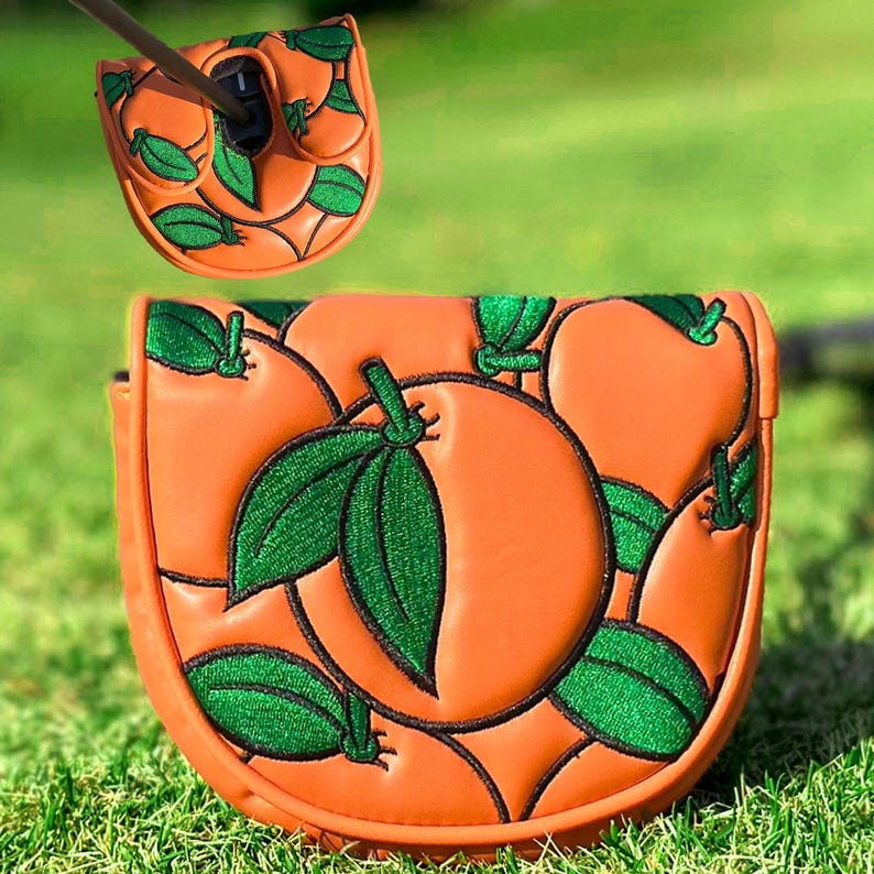 Puede incluir: Funda para putter de palo de golf naranja con dise&ntilde;o de hojas verdes. La funda est&aacute; hecha de un material similar al cuero y presenta un color naranja vibrante con hojas verdes bordadas. El dise&ntilde;o se repite en la cubierta superior.