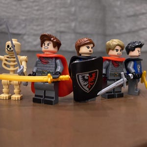 Puede incluir: Un conjunto de minifiguras de Lego que representan caballeros medievales y un guerrero esqueleto. Las figuras visten armaduras, capas y cascos, empu&ntilde;ando espadas y escudos. La paleta de colores incluye gris, rojo, amarillo y negro.