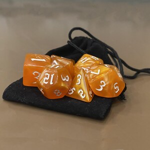 Puede incluir: Un juego de dados naranjas con n&uacute;meros blancos, sobre una bolsa negra con cord&oacute;n. Los dados tienen varias formas, incluyendo un cubo y un dado de 20 caras. Los dados son transl&uacute;cidos.