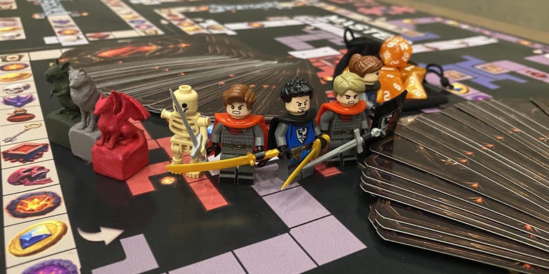 Puede incluir: Un juego de mesa con figuras en miniatura, dados y cartas. El juego presenta figuras de estilo Lego con espadas y capas, junto con otras piezas del juego. El tablero del juego tiene un tema de mazmorra con un dise&ntilde;o de cuadr&iacute;cula.
