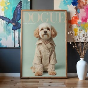 Puede incluir: Un póster de pared enmarcado que muestra a un perro de color claro con una gabardina beige de doble botonadura. El póster tiene un fondo verde claro con el texto DOGUE en la parte superior y texto más pequeño debajo, en un marco de madera fino.
