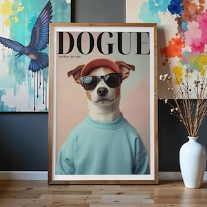 Puede incluir: Una impresión de arte mural enmarcada que muestra a un perro con una sudadera azul claro, una gorra de béisbol color salmón y gafas de sol negras. La parte superior de la impresión muestra el texto DOGUE y First Issue July 2026 en negro.