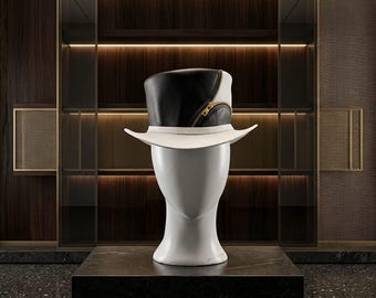 May include: A top hat featuring a black crown and a white brim, accented with a gold-toned zipper detail that curves along the side. The hat is displayed on a smooth, featureless white mannequin head, showcasing its structured design and contrast.