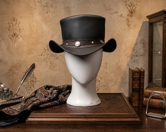 May include: A black top hat featuring a brown leather band adorned with silver-toned circular metal studs and a central emblem. The hat is displayed on a white mannequin head, showcasing a structured crown and a curved brim with a smooth finish.