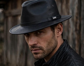 May include: A black leather fedora hat featuring a matching black leather hat band with a small silver-toned metal accent piece. The hat has a pinched crown, a wide brim, and two small metal ventilation eyelets on each side of the crown.