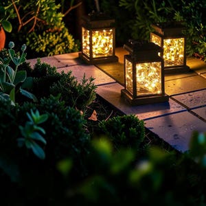 Puede incluir: Tres faroles solares con luces de hadas blancas cálidas iluminan un camino de jardín. Los faroles son de color marrón oscuro, rectangulares y tienen un diseño clásico. El follaje verde rodea los faroles.