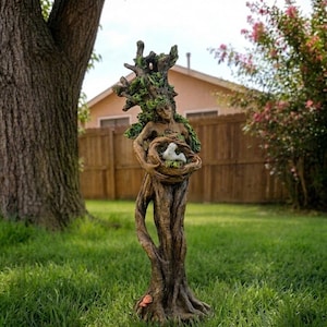 Peut inclure: Une sculpture en forme d'arbre brun représentant une silhouette humaine avec des feuilles vertes intégrées dans les branches. La silhouette tient un nid circulaire contenant un petit oiseau blanc. La base montre des racines et des champignons rouges.