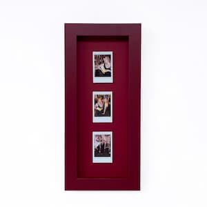 May include: A deep red rectangular shadow box frame containing three vertical instant film photographs arranged in a column. Each photograph features people in social settings, set against a matching deep red mat board background.