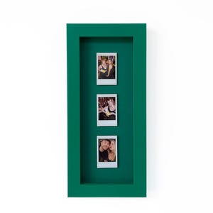 Peut inclure: Un cadre mural rectangulaire profond avec une finition vert foncé unie. Le cadre présente un fond intérieur vert assorti qui contient trois photographies instantanées verticales disposées en une seule colonne, montrant des personnes.