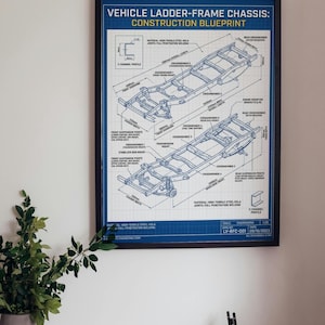 May include: A framed technical blueprint titled VEHICLE LADDER-FRAME CHASSIS: CONSTRUCTION BLUEPRINT. The print features detailed isometric line drawings of a vehicle frame with various components labeled, including crossmembers and mounts.
