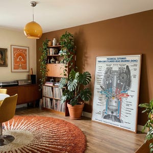 Può includere: Un disegno tecnico in sezione di una testata a doppio albero a camme incorniciato su una parete marrone. La stampa presenta un dettagliato diagramma meccanico in bianco e nero con accenti blu e rossi, linee a griglia ed etichette di testo.
