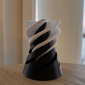 以下が含まれることがあります： ユニークな渦巻き模様の装飾花瓶。花瓶は白と黒の交互の帯があり、らせん状の効果を生み出しています。花瓶は丈夫な素材でできており、木製の表面に置かれています。