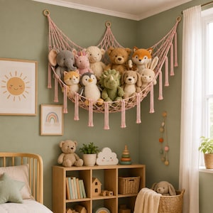 May include: A pink macrame corner hammock suspended from the wall, filled with a collection of plush stuffed animals including an elephant, a unicorn, a bear, a fox, a penguin, a dinosaur, and a rabbit, featuring knotted rope and hanging tassels.