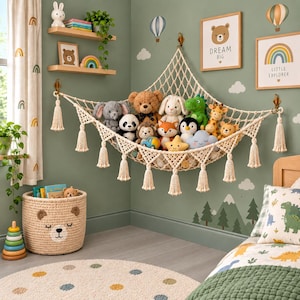 Op de afbeelding: Een crèmekleurige macramé speelgoedhangmat met decoratieve kwastjes, gemonteerd in een hoek en gevuld met diverse knuffels, waaronder een teddybeer, olifant, panda, vos, pinguïn en dinosaurus, als opbergoplossing voor zacht speelgoed.