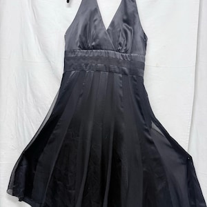 May include: A black knee-length halter dress featuring a satin bodice with a V-neckline, a wide horizontal banded waist, and a flared skirt composed of alternating panels of solid satin fabric and sheer, lightweight material.
