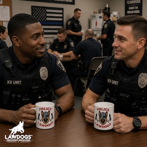 May include: Two police officers in uniform are seated at a table, each holding a white mug. The mugs display the text "POLICE LAWDOGS" with a dog graphic. The officers are in a room with other officers and an American flag.