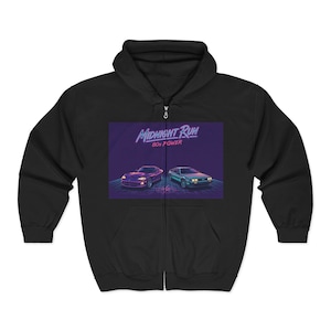 Op de afbeelding: Zwarte hoodie met ritssluiting met een retro afbeelding van twee auto's en de tekst "Midnight Run 80s Power". De afbeelding gebruikt paarse, blauwe en turquoise kleuren. De hoodie heeft een capuchon en een ritssluiting aan de voorkant.