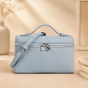 May include: A light blue rectangular handbag with a textured pebble grain finish. The bag features a top handle, a thin adjustable shoulder strap with a silver buckle, and a silver-toned zipper closure with two matching metal zipper pulls.