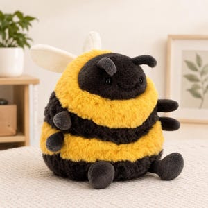May include: A plush bee toy with a round, fuzzy body featuring alternating horizontal stripes of black and yellow. The stuffed animal has two small antennae, two white wings on its back, and four small limbs extending from its sides and base.