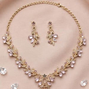 Peut inclure: Un ensemble collier et boucles d'oreilles doré composé de motifs de feuilles en métal délicat ornés de cristaux rose clair en forme de goutte et ronds. Le collier présente un pendentif central et les boucles d'oreilles sont des motifs pendants.