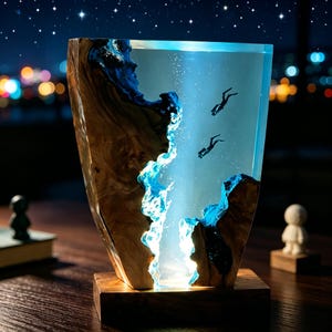 May include: A decorative lamp made from wood and resin, depicting a marine scene with two divers. The lamp has a wooden base and a clear resin body with blue detailing, creating an underwater effect. The lamp is illuminated from within.