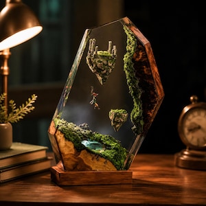 May include: A unique resin art piece featuring a miniature fantasy landscape. The clear resin encases floating islands with miniature castles and figures, surrounded by moss and a wooden base. The artwork is illuminated by a warm light.