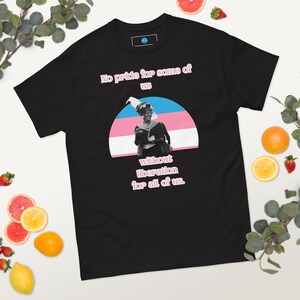 Peut inclure: T-shirt noir avec le texte "No pride for some of us without liberation for all of us." Le t-shirt présente un graphisme d'une personne devant un drapeau de la fierté transgenre.