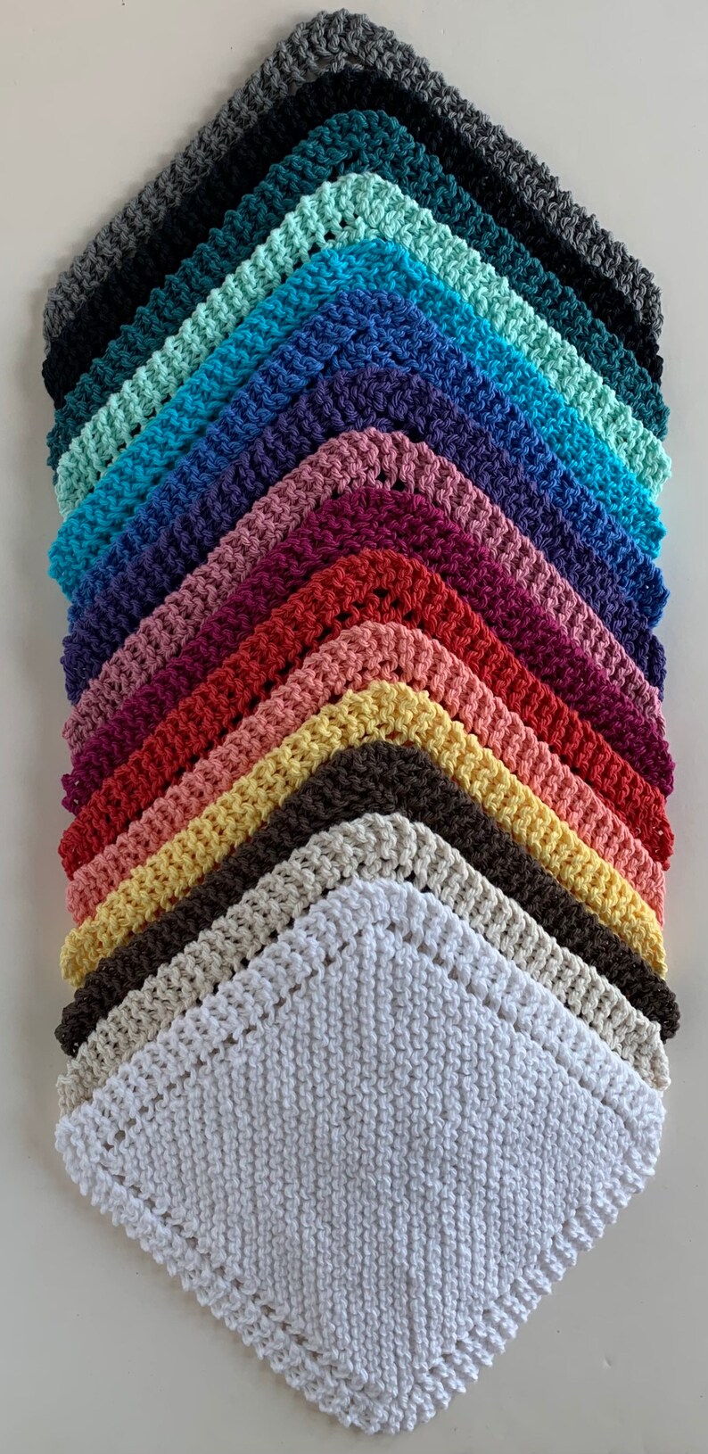 Puede incluir: Una pila de 12 pa&ntilde;os de cocina de ganchillo en varios colores, incluyendo blanco, beige, amarillo, naranja, rojo, rosa, morado, azul, turquesa y gris. Los pa&ntilde;os de cocina est&aacute;n dispuestos en forma triangular, con el pa&ntilde;o de cocina blanco en la parte inferior.