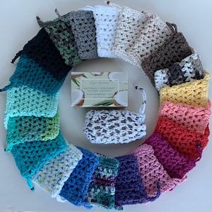 May include: A variety of colorful crocheted soap savers in different patterns and colors. The soap savers are arranged in a circle around a bar of soap labeled "Oatmeal + Coconut Plant-Based Scented Soap".