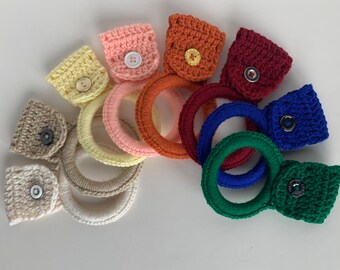 May include: A set of eight crocheted dishcloths with a pocket and button. The dishcloths are in various colors, including beige, yellow, pink, orange, red, blue, and green.