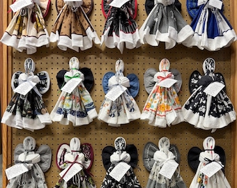May include: A collection of fifteen decorative angel ornaments crafted from folded kitchen towels and potholders. Each figure features a fabric towel body, a potholder wing set, and a small white tag tied with string around the neck area.