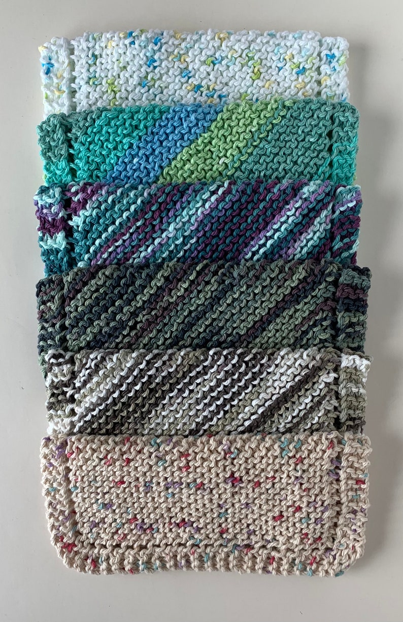Puede incluir: Una pila de seis pa&ntilde;os de cocina de punto en varios colores y patrones, incluyendo blanco con motas amarillas, rayas verdes y azules, rayas moradas y azules, verde oscuro, rayas grises y blancas, y beige con motas multicolores.